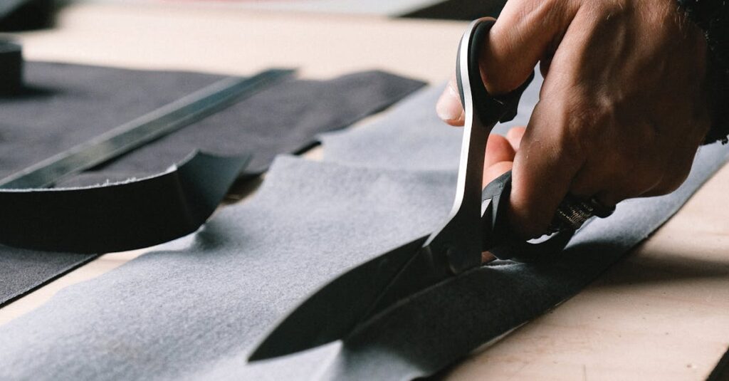 A tailor precisely cuts fabric on a workbench with professional scissors.