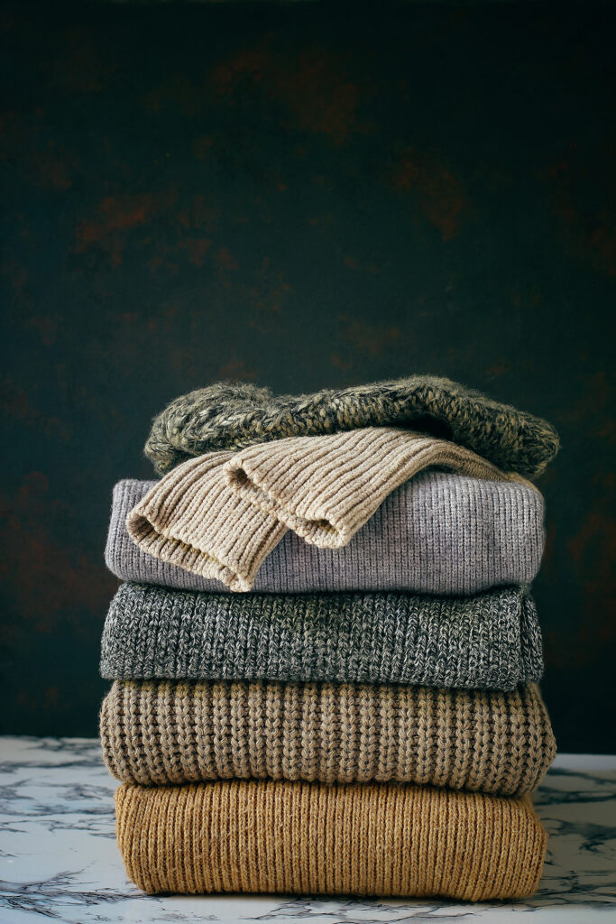 stack of cozy knitted sweaters on wooden background. autumn wint